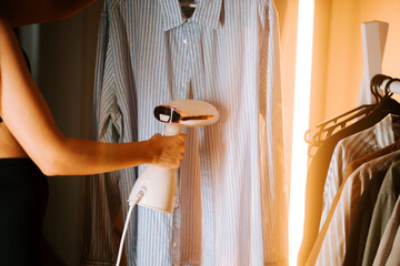 Woman using garment steamer to press shirt in cozy room during daylight