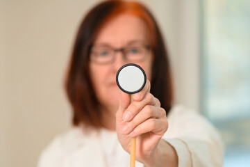 Mature doctor in white medical clothing uses stethoscope diaphragm during chest examination. Focus...