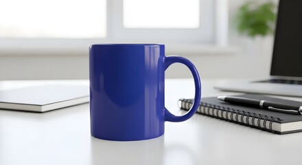 A vibrant blue ceramic mug sits prominently on a clean white desk, surrounded by office essentials like a laptop, notebook, and pen, with a bright window in the background.