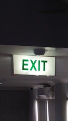 Illuminated green EXIT sign on the ceiling of a building, indicating an emergency exit route....