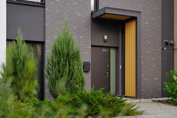 Modern residential building with dark brick facade, featuring black door with vertical glass panel,...