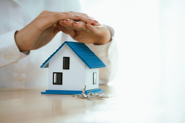 Hands carefully hold and shield a small house model, symbolizing protection, home insurance,...