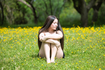 Young, dark and beautiful woman sitting in a green meadow with yellow flowers. The woman is hugging...