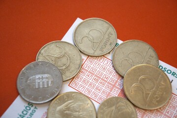 Close-up view of a Hungarian lottery ticket with scattered forint coins. Concept of luck, gambling,...
