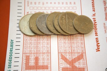 Close-up view of a Hungarian lottery ticket with scattered forint coins. Concept of luck, gambling,...
