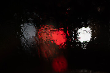 Abstract background of blurred red and white city lights seen through a wet, rainy window at night....