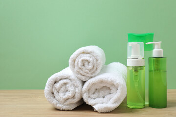 White towel and bathroom toiletries on wooden table with green background
