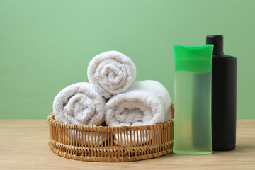 White towel and bathroom toiletries on wooden table with green background
