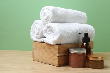 White towel and bathroom toiletries on wooden table with green background
