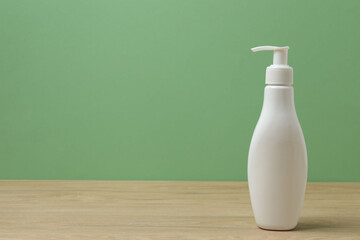 White bottles of toiletries on a wooden table with a green background