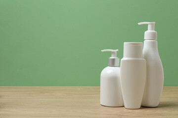 White bottles of toiletries on a wooden table with a green background