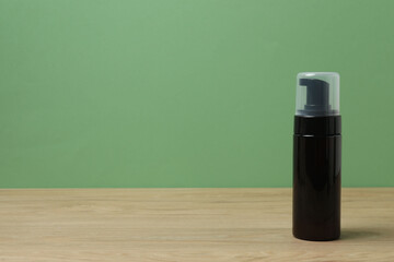 Black bottles of toiletries on a wooden table with a green background
