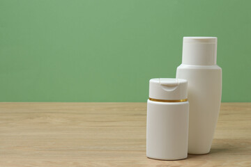 White bottles of toiletries on a wooden table with a green background