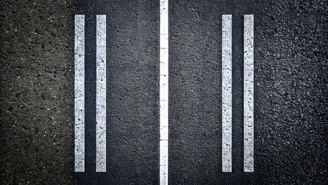 A high angle view of a dark asphalt road with clear white lane markings showing a central solid white line flanked by two sets of double white lines