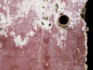 A red maroon and white rustic walls with a round hole and cracks.