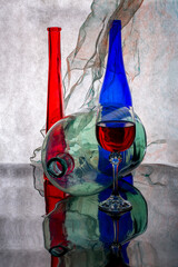 Still life with a blue and red bottle, a glass of wine and a glass jar