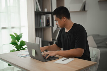 Young man working on laptop at modern desk in bright home office, focusing on tasks surrounded by plants and organized workspace, productivity and creativity.
