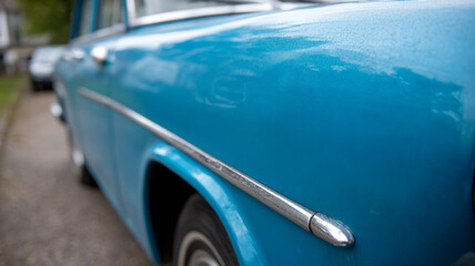 Close-up of a blue vintage car's side with chrome detailing.