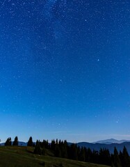 Naklejka premium Night sky with a vast expanse of stars above a dark mountain range