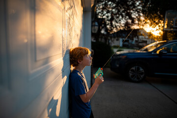 Child sprays water across driveway lit by sunset glow