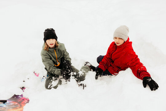 Two young boys playing in snow after sledding downhill