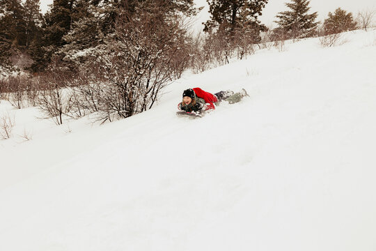 Friends sledding down snowy hill in winter forest