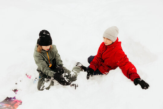 Two youngsters playing in fresh snow after sledding downhill