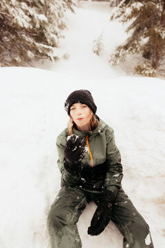 Young boy eating snow while sitting in snowy woods