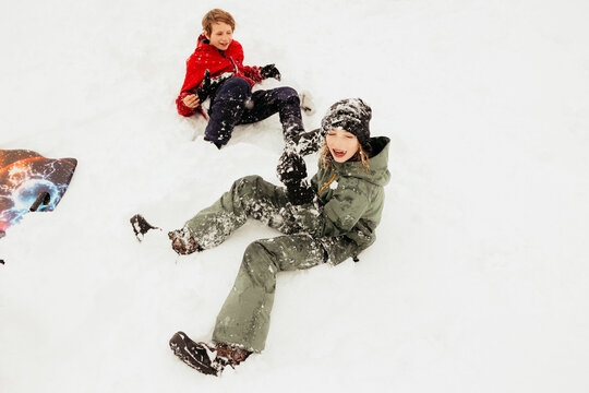 Two boys laughing and playing in the snow after sledding