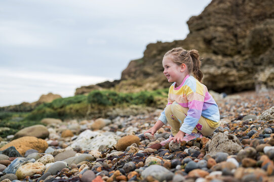 Family holiday at seaside. Little girl picking stones at the beach