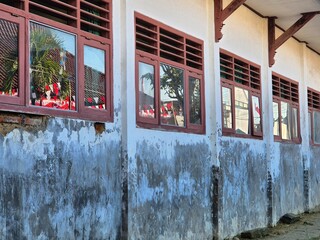 Weathered wall of old school building with brown wooden windows and flag indonesia reflections