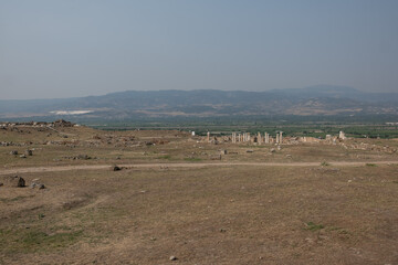 Fototapeta premium Exploration of the extensive ruins of Laodikeia reveals remnants of ancient structures set against a backdrop of rolling hills and open terrain