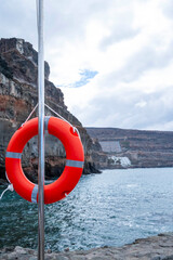 A red life preserver is hanging from a pole in the ocean. The scene is calm and peaceful, with the...