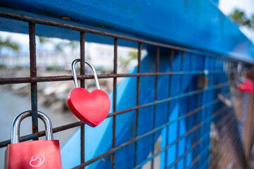 A blue fence with red hearts on it. The hearts are attached to a metal gate. The gate is locked...