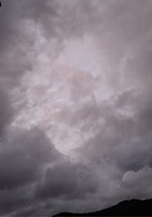 Fototapeta premium dark rain clouds float across the blue sky, evening, sunset, lightning illuminates the storm clouds, a landscape with clouds and mountains, and trees