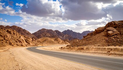 Winding road through desert mountains under a partly cloudy sky