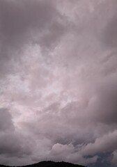  dark rain clouds float across the blue sky, evening, sunset, lightning illuminates the storm clouds, a landscape with clouds and mountains, and trees
