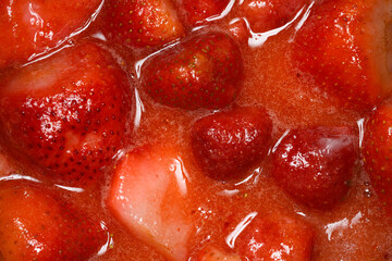 A close-up of strawberries and sugar cooking in a pot, capturing the process of making homemade...