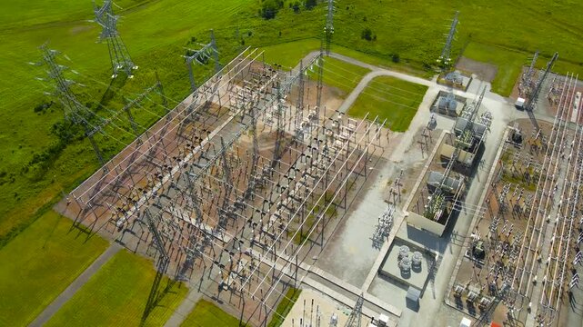 Aerial drone footage orbiting around a modern electrical substation power station during a sunny day in a rural countryside with high voltage and dangerous power cables and transformers, control room.