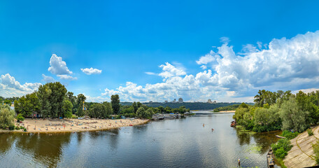 A large recreational area in the middle of the river. Wide banner with copy space. Long city sandy beach with infrastructure. A row of clouds beautifully organized in the sky.