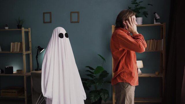 Depressed man grieving over loss of loved one standing at window ghost of his wife standing nearby comforting husband