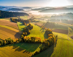 Widok z góry na spowite w lekkiej mgle zielone pola uprawne, łąki i drzewa o wschodzie słońca