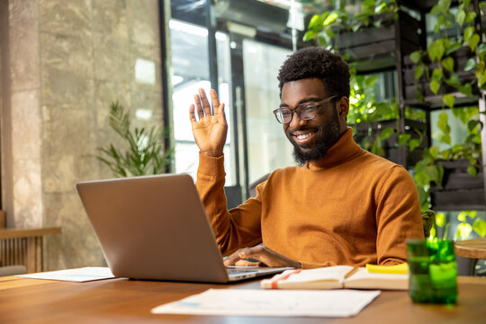 Bearded male professional waving hand on video call communicating with team from office
