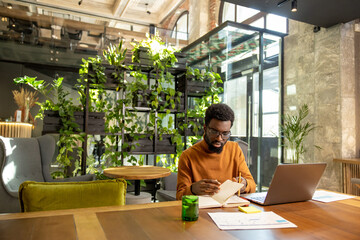 Fototapeta premium Focused African American man using laptop for distance work in urban modern interior
