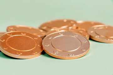 Heap of golden casino coins with a subtle texture on a light green surface. Gambling and betting concept and symbol