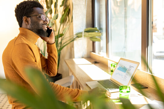 Businessman multitasking at modern workspace speaking on mobile phone and typing on laptop in office
