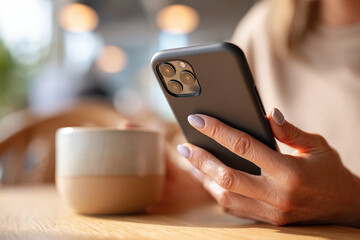 Female hand holding smartphone and cup of coffee in cozy cafe setting during afternoon