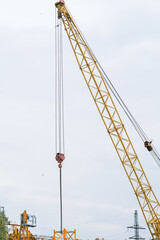 Fototapeta premium Moscow, Russia, 18.06.2025 Yellow construction crane boom with hook against a cloudy sky. Industrial equipment for heavy lifting at a construction site.
