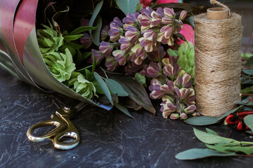 flowers bouquet in wrapping paper, thread, and scissors on a wooden table