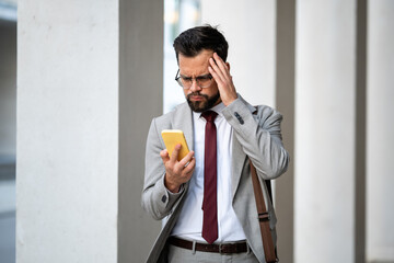Stressed businessman reading bad news on smartphone touching head